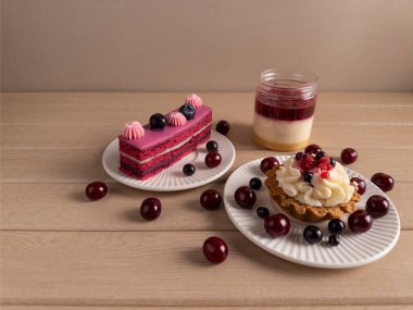 Beyaz tabakta taze kiraz ve yaban mersini ile süslenmiş katmanlı kek, tart ve kavanoz tatlıdan oluşan görsel olarak çekici bir tatlı çeşidi.