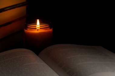 Cam kavanozdaki bir mumun sıcak parıltısıyla aydınlatılan açık bir kitapla huzurlu bir sahne, rahat ve düşünceli bir atmosfer yaratıyor. Yalnızlık, okuma, gece rutini ve yavaş yaşam kavramları için ideal.