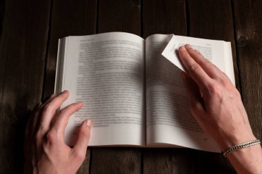 Erkek ellerinin, koyu ahşap bir masada bir kitabın sayfasını çevirdiği yakın plan. Okuma, edebiyat, eğitim, öğrenme ve bilgi kavramı