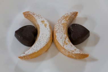 Şeker tozlu kurabiye ve kalp şeklinde siyah çikolata ile beyaz tabak, pişirme, tatlı ve romantik temalar için ideal.