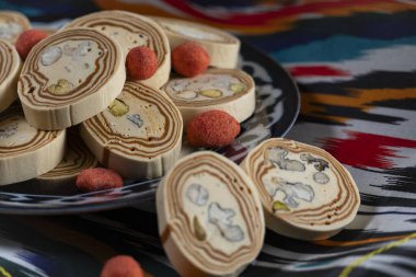 Geleneksel Özbek seramik tabağa konmuş şam fıstıklı ve baharatlı halva renkli ulusal kumaş, sergilenen kültür mirası ve gurme cazibesi