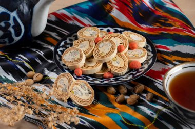 Antep fıstığı ve baharatlı fıstıkla kaplı Özbek irmik halkasının geleneksel seramik tabakta canlı Özbek kumaşına karşı yakın plan fotoğrafı.