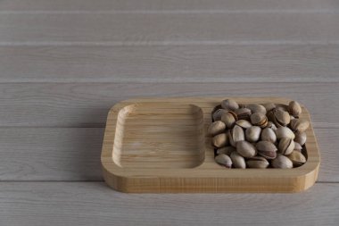 Tahta bir tepside, ahşap bir yüzeye serpilmiş, doğal dokuları ve toprak tonlarını ön plana çıkaran, kırsal kabuklu şam fıstığı manzarası.