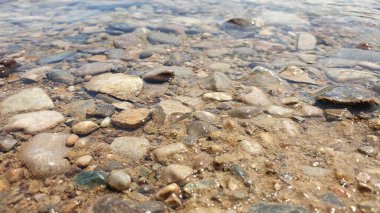 Pürüzsüz nehir taşlarının üzerinden akan temiz sığ su doğal ve ferahlatıcı bir doku yaratır. Güneş ışığı ıslak kayalardan yansıyarak renklerini ve detaylarını vurgular. Doğa arkaplanı ya da doku olarak mükemmel