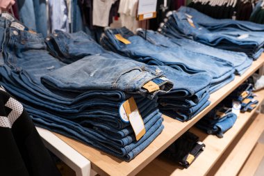 Bir giyim mağazasındaki ahşap raflarda düzgünce dizilmiş mavi kot yığınları, perakende satış ve satış konsepti sergileniyor.