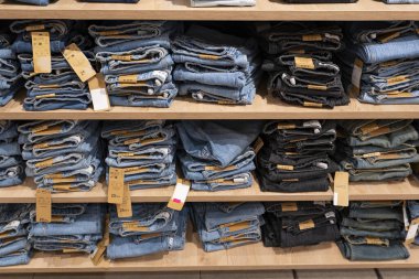 Bir giyim mağazasındaki ahşap raflarda düzgünce dizilmiş mavi kot yığınları, perakende satış ve satış konsepti sergileniyor.