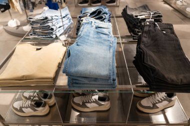 Bir giyim mağazasındaki ahşap raflarda düzgünce dizilmiş mavi kot yığınları, perakende satış ve satış konsepti sergileniyor.