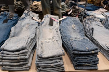 Bir giyim mağazasındaki ahşap raflarda düzgünce dizilmiş mavi kot yığınları, perakende satış ve satış konsepti sergileniyor.