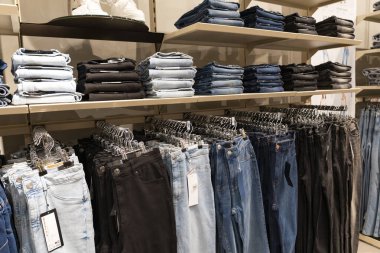 Bir giyim mağazasındaki ahşap raflarda düzgünce dizilmiş mavi kot yığınları, perakende satış ve satış konsepti sergileniyor.