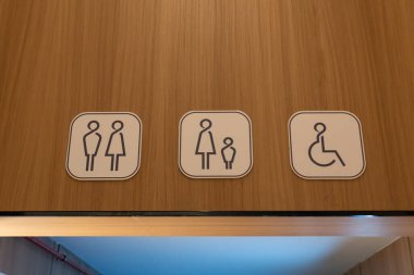 Kare tuvalet ve erişilebilirlik tabelaları beyaz arka planda mavi ikonlar, ahşap bir duvara monte edilmiş, uniseks, aile ve tekerlekli sandalyeye ulaşılabilir tesisleri gösteriyor