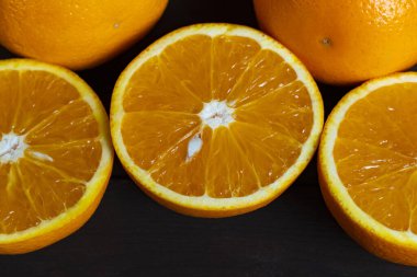 Sulu olgun portakallar ve koyu ahşap bir masada yarıya indirilmiş narenciye meyveleri. Taze, sağlıklı ve canlı tropikal meyve. Yemek, diyet ve vitamin konsepti için mükemmel.