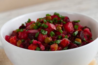 Homemade Russian beetroot salad vinaigrette served in a white bowl with bread, pickles and green onion. Traditional healthy vegetarian dish