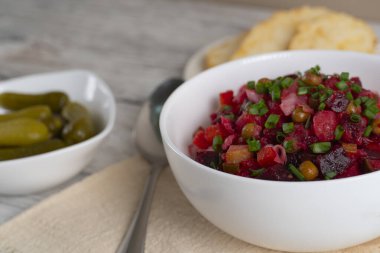 Homemade Russian beetroot salad vinaigrette served in a white bowl with bread, pickles and green onion. Traditional healthy vegetarian dish
