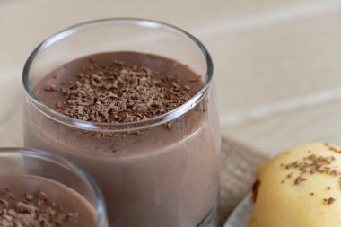 Cam bardaklarda çikolatalı pudingle servis edilen nefis ev yapımı kurabiyeler, üstüne de rendelenmiş siyah çikolata. Ahşap masada sıcak tatlı kompozisyonu