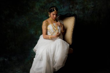 Tek başına, beyaz sari giyen, altın takılar takan, yeşil, saf bir arka planda altın bilezik takan Hintli bir kadın resmi.