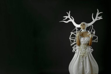 Geyik boynuzu gibi görünen beyaz bir taç giyen beyaz elbiseli bir manken..