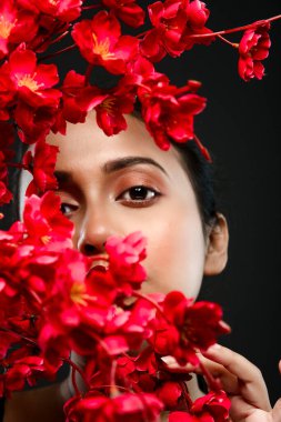 Stüdyoda çekilen bir demet kırmızı çiçeğin arkasında siyah bir arkaplan önünde güzel bir kadın mankenin yüzü.