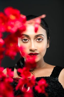 Stüdyoda çekilen bir demet kırmızı çiçeğin arkasında siyah bir arkaplan önünde güzel bir kadın mankenin yüzü.
