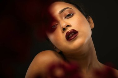 Stüdyoda çekilen bir demet kırmızı çiçeğin arkasında siyah bir arkaplan önünde güzel bir kadın mankenin yüzü.