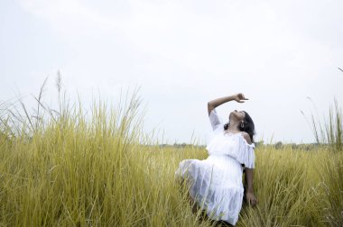 Siyah saçlı, buğday tenli, beyaz etekli ve açık çim tarlasının ortasında poz veren genç bir Hintli kadın model.