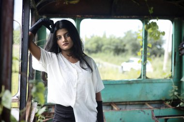 Terk edilmiş bir otobüsün içinde beyaz gömlekli ve siyah pantolonlu bir kadın model.