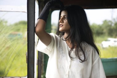 Terk edilmiş bir otobüsün içinde beyaz gömlekli ve siyah pantolonlu bir kadın model.