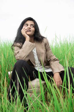 Siyah saçlı, buğday tenli, beyaz tişörtlü, siyah pantolonlu, açık çim tarlasının ortasında poz veren Hintli genç bir manken.