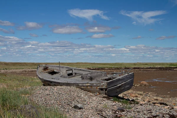 Arviat, Nunavut, Kanada 'nın kuzeyinde kayalık bir kıyı şeridinde batmış eski ahşap teknenin yan görüntüsü.
