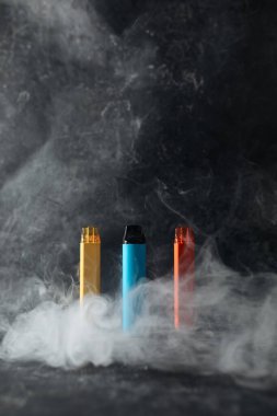 Üzerinde sigara dumanı olan bir masanın üzerinde, arka planda duran tek kullanımlık elektronik sigara seti. Modern sigara, buhar ve nikotin konsepti
