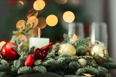 Bir mum, kırmızı ve altın süslemeli kompozisyon. Noel ve Yeni Yıl konsepti, iç ayrıntılar, köknar ağacının arka planında seçici aksan ve bokeh etkisi.