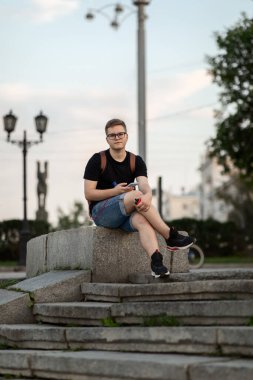 Gözlüklü, sıradan giyimli, omuzlarında sırt çantası olan yakışıklı bir genç adam. Şehrin sokaklarında gezen bir öğrenci.