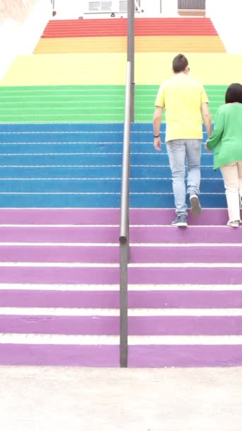 カラフルな階段を歩いて若いカップル 登山や通りのバックパックで虹の階段を登る 概念自由権抽象的隠喩垂直ビデオ 高画質映像 — ストック動画