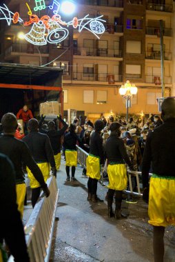 Ibi, Spain - January 5th 2022. Royal parcel drivers carrying packages and gift boxes on ladders to climb the balconies. Vertical. Page Magi parade in Epiphany eve tradition.