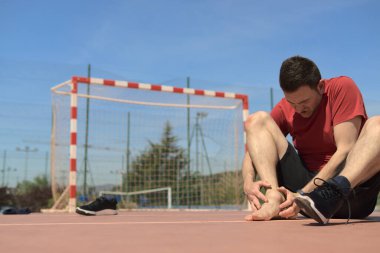 Atletizm antrenörü yaralı eklemlerini hissediyor. Ayakkabılarını çıkar. Diğer bacak onun önündeydi. Uzay renkli resmini kopyala. Spor tıbbı ve fizik tedavi konsepti. Yüksek kalite fotoğraf