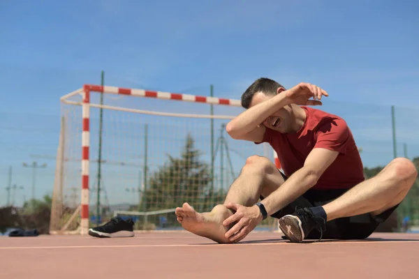 sore man with swollen ankle from injury playing soccer covers his face with his arm while screaming. Has taken off his shoe. Sports physiotherapy medicine concept. High quality photo