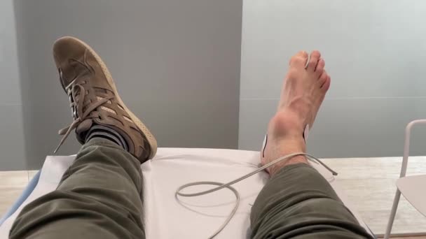 人的脚 右脚有肿胀的踝关节发炎 在事故后躺在医疗诊所的担架上 并与电疗电缆连接以恢复 电磁疗法 — 图库视频影像