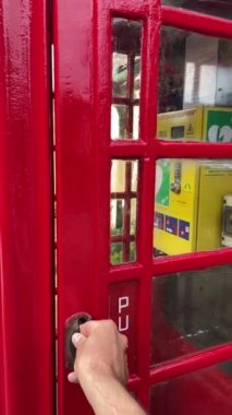 İngiltere 'de Defibrilatör kabinine dönüştürülmüş kırmızı bir telefon kulübesinin kapısını açan bir adam. Community Heartbeat Trust, yenilik fikrini ortaya atan bir hayır kurumu. Dikey 4k