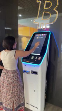 Alicante, İspanya - 29 Temmuz 2023. Bitcoin ATM 'de işlem yapan ya da satan genç bir kadın. Ekonomik bağımsızlığı kripto para birimine yatırım olarak kabul et. Dikey ağır çekim 4K