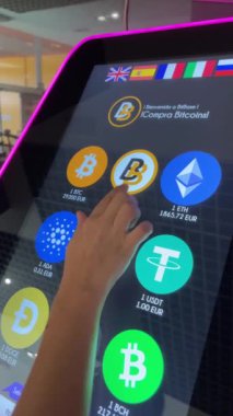 Alicante, İspanya - 29 Temmuz 2023. Genç bir kadın alışveriş merkezindeki ATM 'den şifreli para seçiyor. Yatırımcı insan konsepti. Dikey yakın çekim 4k bitcoin, ada, cardano, btc, litekoin, ethereum 