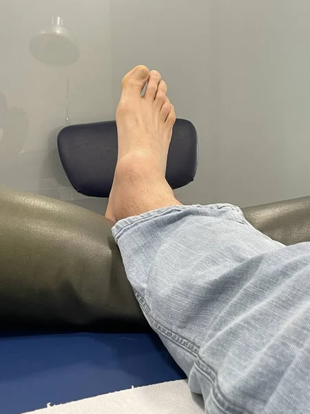 Feet of man. Right foot with swollen ankle inflamation, lying on a medical clinic stretcher after having an accident, with Electrotherapy cables connected to recover. Electromagnetic therapy