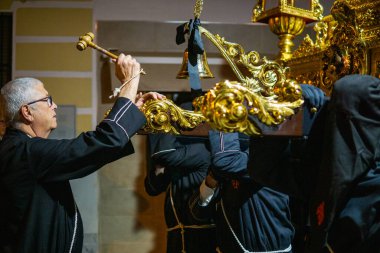 April 7th 2023 - Dona Mencia, Cordoba, Spain. Hermano Mayor, Big Brother of a brotherhood knocking the bell of a Holy Week step to give an order to the costalero bearers. Black robe and wooden hammer clipart