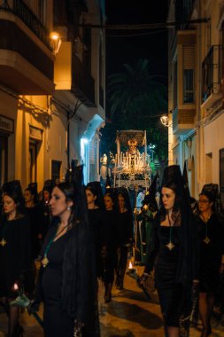 April 8th 2023 - Dona Mencia, Cordoba, Spain. The Virgin of Solitude under Canopy, Virgen de la Soledad illuminated by candles. Women dressed in black with headwear and mantilla shawl. Vertical shot clipart