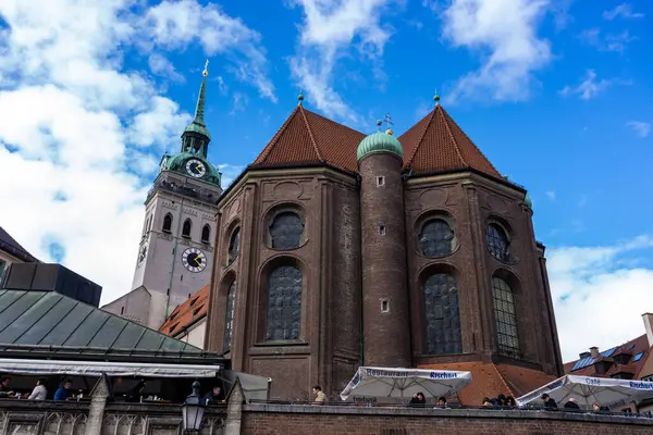 16 Mart 2024 - Münih, Almanya. St. Peter Kilisesi, Peterskirche, Viktualienmark manzaralı. Restoran ve barların yanındaki antik mirasın aksine. Şehirde yiyecek ve içecek var.