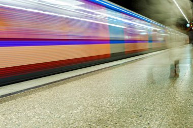 Tren bulanık bir arkaplanla raylarda ilerliyor. Tren renkli ve hızlı hareket ediyor.