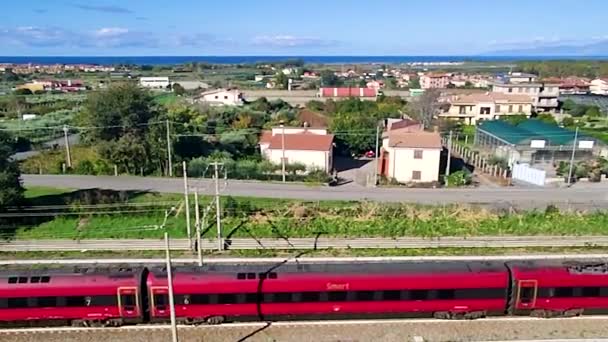 从空中看红色火车 高速列车的运行 旅客列车通过农村铁路 美丽的夏日背景与大海遥相望 — 图库视频影像