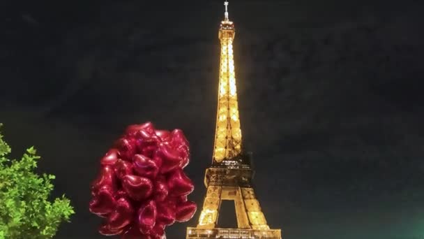 パリのエッフェル塔の前の赤いハート型の風船の山フランスの夜 エッフェル塔と暗い空に対して手描きの風船の低角度ビュー — ストック動画