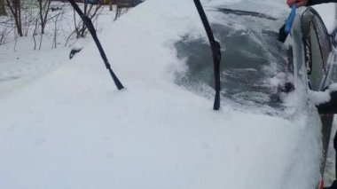 A Man Removes Snow From the Windshield of a Car. Cleaning the Side Windows of the Car From Snow and Ice Before the Trip. A Man's Hand Cleans a Car with a Special Tool on a Snowy Frosty Winter Day.