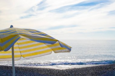 Striped Beach Umbrella on the Beach. Colorful Umbrella and Beach with Warm sea on a Sunny day on a Beach in Southern Italy. The Concept of Nature and Travel.