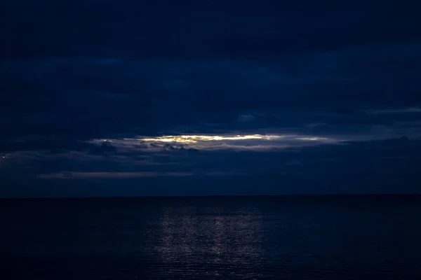 Night Clouds Over the Water. The Light from the Full Blue Moon Breaks Brightly Through the Clouds and Rises over the Calm Ocean, Creating Sparks on the Waves. Moon Path Over the Ocean.
