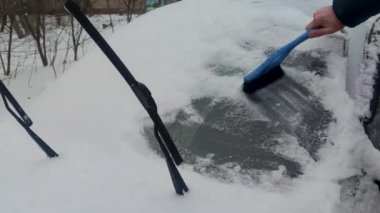 Kar fırtınasından sonra sabah bir adam arabayı kardan temizler. Kış Sezonu.